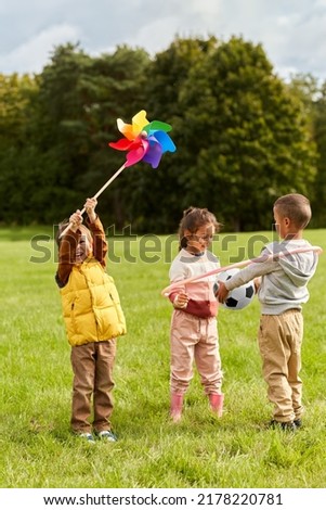 childhood, leisure and people concept - happy kids with pinwheel having fun at park Royalty-Free Stock Photo #2178220781