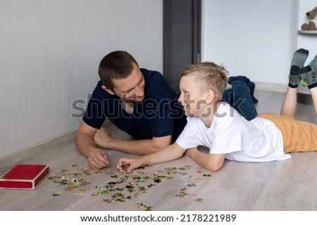 A cute boy with a cheerful dad is collecting a puzzle lying on the floor in a room