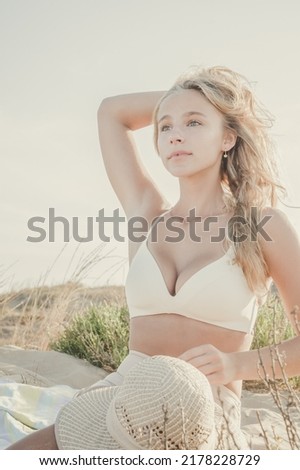 Young attractive blonde woman in bikini enjoys a day at the beach posing touching her hair on the mediterranean coast. Summer warm colors.