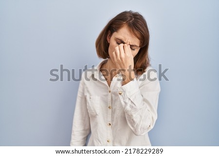Young beautiful woman standing casual over blue background tired rubbing nose and eyes feeling fatigue and headache. stress and frustration concept. 