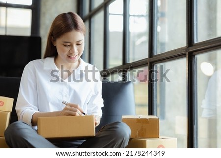 Woman who runs an e-commerce business is writing a list of customers on paper before shipping to them, she runs an e-commerce business on websites and social media. Concept of selling products online.