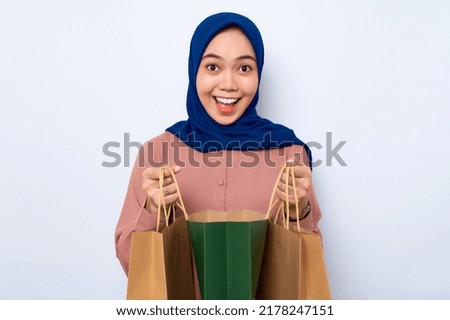 Cheerful young Asian muslim woman in pink shirt opening  package bags with purchases after shopping isolated over white background. People lifestyle concept