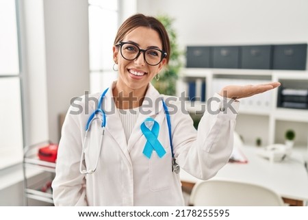Young brunette doctor woman wearing stethoscope at the clinic smiling cheerful presenting and pointing with palm of hand looking at the camera. 