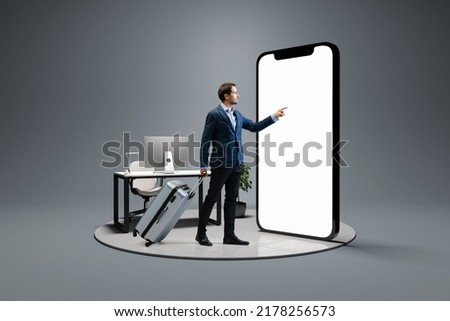 Booking business trip online. Young man, businessman standing in front of 3d model of cellphone with blank white screen isolated on grey background. On-line shopping, trip, travel, ad, sales, Royalty-Free Stock Photo #2178256573