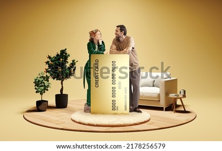 Modern lifestyle. Happy family couple standing near to huge 3d model of credit card at home interior isolated on golden color background. New app, mortgage, lending, ad concept