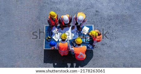 Top view of team of architectural engineer working, meeting, planning with blueprint, Solar photovoltaic equipment, wind turbine business important infrastructure on solar panel at construction site.  Royalty-Free Stock Photo #2178263061