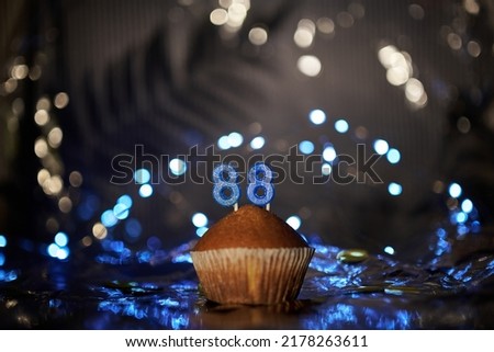 Digital gift card birthday concept. Tasty fresh homemade vanilla cupcake with number 88 eighty eight on aluminium foil and blurred dark background in minimalistic style. High quality image