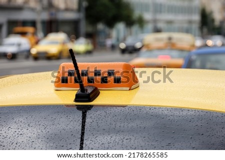 Taxi top sign and antenna on yellow car roof with raindrops on road background, rain in city