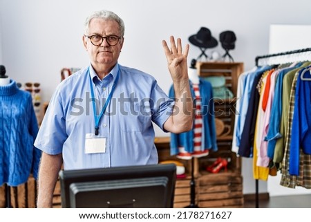 Senior man with grey hair working as manager at retail boutique showing and pointing up with fingers number four while smiling confident and happy. 