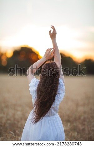 Young beautiful woman 19-20 years old with dark hair in a white boho style dress in a wheat field at sunset. Summer happy young model portrait. Summer.