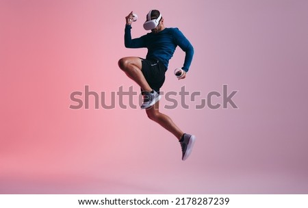 Man playing a game of kickboxing in virtual reality. Active young man jumping mid air while wearing virtual reality goggles. Sporty young man exploring immersive virtual reality games. Royalty-Free Stock Photo #2178287239