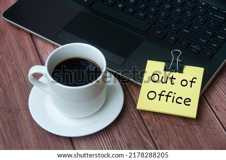 Coffee cup and laptop on wooden table with yellow notepad with text - Out of office. Business concept