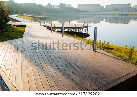 Morning in the city park, a pedestrian road of boards runs along the lake, a round pier for boats, a wooden pier on the water, the design of the park in nature. High quality photo Royalty-Free Stock Photo #2178292821
