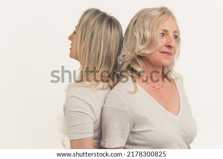 Two bloned-haired focused peaceful women in their 40s standing back to back, looking dreamy, wearing white t-shirts. High quality photo