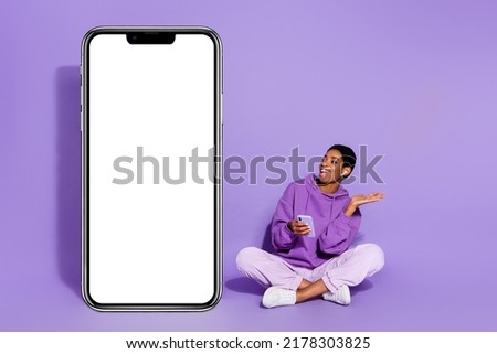 Photo of excited music lover transgender person hold phone listen music wear violet hoodie isolated purple color background