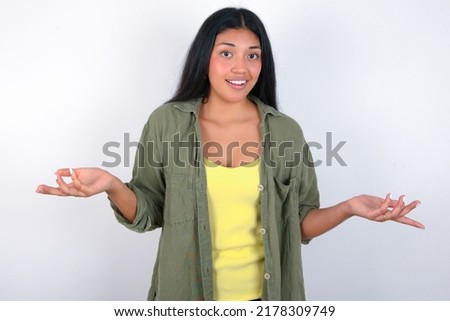 So what? Portrait of arrogant Young hispanic woman wearing green jacket over white background shrugging hands sideways smiling gasping indifferent, telling something obvious. Royalty-Free Stock Photo #2178309749
