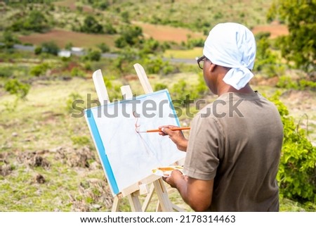 artist painting or drawing on canvas board by seeing mountians and nature at top of hill - concept of hobbies, leisure activities, creativity.