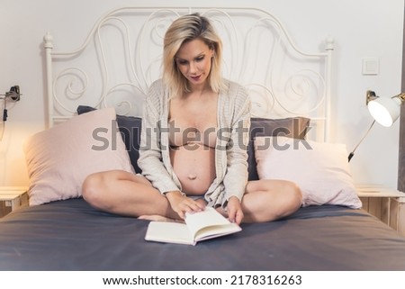 pregnant woman sitting on the bed and reading an interesting book, full shot bedroom pregnancy concept. High quality photo