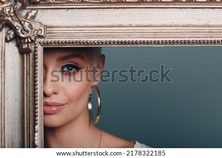 Millenial young woman with short blonde hair holds gilded picture frame. Museum restoration recovery renewal picture frame for painting art