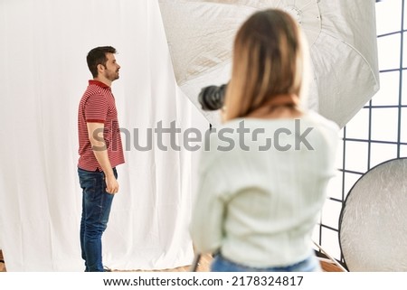 Woman photographer talking pictures of man posing as model at photography studio looking to side, relax profile pose with natural face with confident smile. 