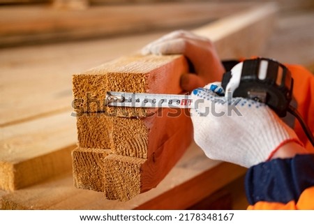 Wooden boards in a warehouse of building materials. Measuring the board with a ruler. Stacked lumber. With hand. Closeup wooden boards, with a shallow depth of field, close up