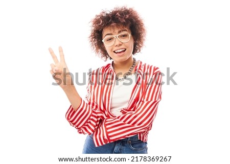 Positive friendly kazakh girl with afro hairstyle shows peace and love gesture wishes good luck to everyone isolated on studio background