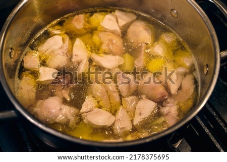 Close-up of broth in a steel pot on the stove, pieces of white chicken meat are boiled in a pot, hot broth for soup top view