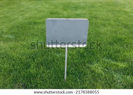 Closeup gray metal sign at green grass background, nameplate with a space for your text. Horizontal banner