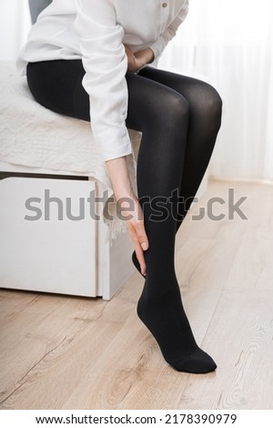 Girl putting on stockings at home. Black compression stockings on a woman in a white room. Black tights. Beautiful female legs.