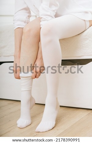 Girl putting on white stockings at home. Anti-embolic stockings. Compression Hosiery. Medical stockings, tights, socks, calves and sleeves for varicose veins and venouse therapy.