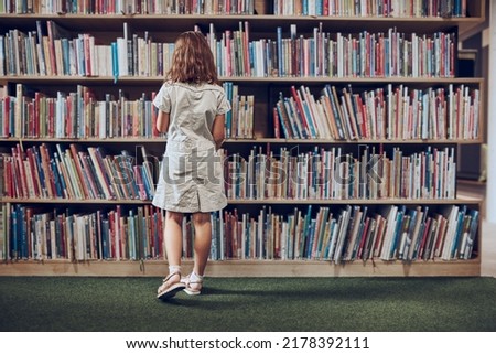 Schoolgirl choosing book in school library. Smart girl selecting literature for reading. Books on shelves in bookstore. Learning from books. School education. Benefits of everyday reading Royalty-Free Stock Photo #2178392111