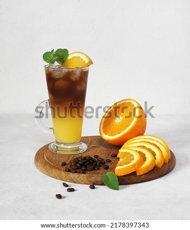 Glass of colorful cocktail bumble bee with orange juice and espresso coffee on white table with fresh oranges. Trendy summer coffee drink. Menu, recipe. Copy space for text