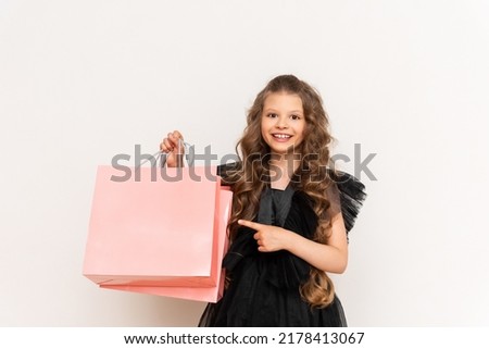 A joyful girl in a dress holds a shopping bag on Black Friday. Shopping for a little princess with curly hair on a white isolated background.