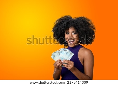 woman holding money, young smiling woman holding Brazilian money, orange gradient background