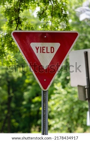 Red Yield Sign on Blurred Green Trees Background