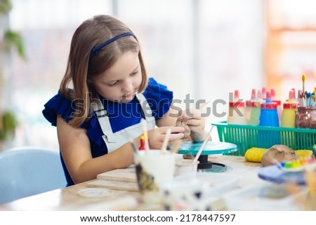 Child working on pottery wheel. Kids arts and crafts class in workshop. Little girl creating cup and bowl of clay. Creative activity for young children in school. Cute kid forming toy with ceramic.  Royalty-Free Stock Photo #2178447597