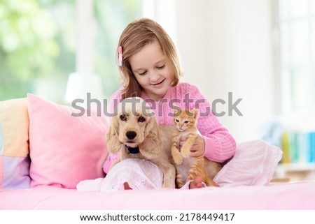 Child playing with baby dog and cat. Kids play with puppy and kitten. Little girl and American cocker spaniel on bed at home. Children and pets at home. Kid taking nap with pet. Animal care.