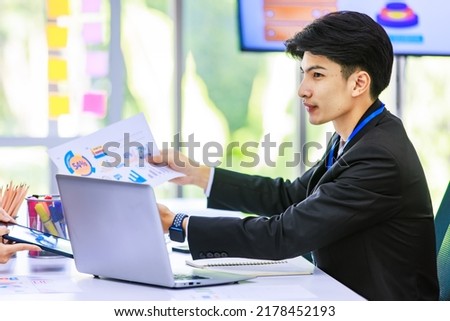 Asian young handsome professional success male businessman employee staff in formal suit sitting working with laptop notebook computer and paperwork graph chart growth target document in meeting room.