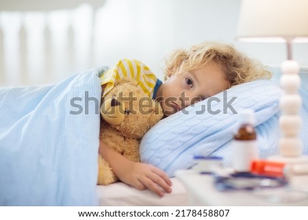 Sick little boy with asthma medicine. Ill child lying in bed. Unwell kid with chamber inhaler for cough treatment. Flu season. Bedroom or hospital room for young patient. Healthcare and medication. Royalty-Free Stock Photo #2178458807