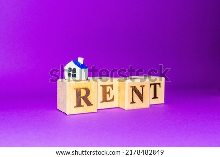 Wooden cubes with word RENT with miniature toy house on a pink background.