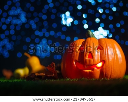 Against the backdrop of a blue starry sky Halloween composition. A large orange pumpkin with a carved face, a smile, illuminated from the inside on a green lawn, fruits and cones.
