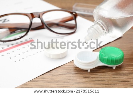 Dripping solution into case with contact lenses on wooden table, closeup