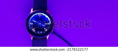 Smart watch on wireless charging with on-screen.Purple,veri peri neon,glowing trendy color background.Top view.Copy space.Banner,advertisement.Indoors shot.