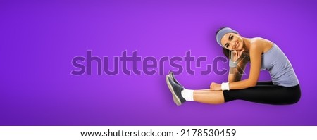 Happy smiling african american woman in sportswear doing fit stretching exercise or youga moves, isolated on violet purple background. Young sporty model at studio shot. Fitness concept.