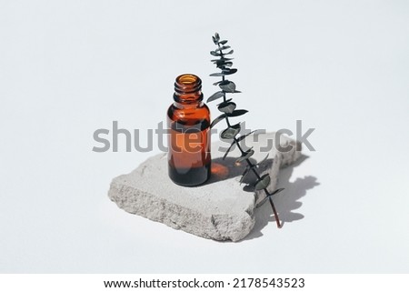 Open amber bottle without cap with eucalyptus branche. White background with daylight and beautiful shadows. Skincare serum or essential oil natural cosmetic. Beauty concept for face and body care Royalty-Free Stock Photo #2178543523