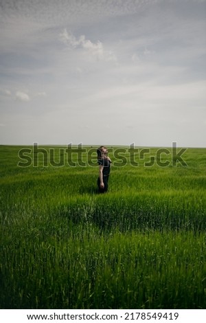The portrait of beautiful cute woman no makeup in black shirt stand on green grass of wheat field. Sunny summer day, girl, blue sky, wild nature, mood vacation, relax. Be free, to love earth.