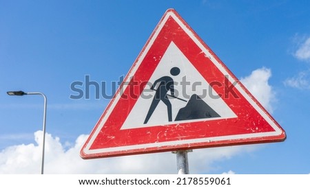 Road works sign, under construction. Red road sign with working man with a blue cloudy sky at the background