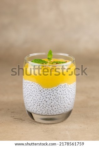 Chia seed pudding, coconut milk and mango puree in a glass cup. Close-up, on a beige background. Selective focus. Raw, vegan, sugar-free desserts. High quality photo