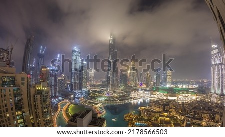 Skyscrapers rising above Dubai downtown night timelapse, mall and fountain surrounded by modern buildings aerial top panoramic view with cloudy sky