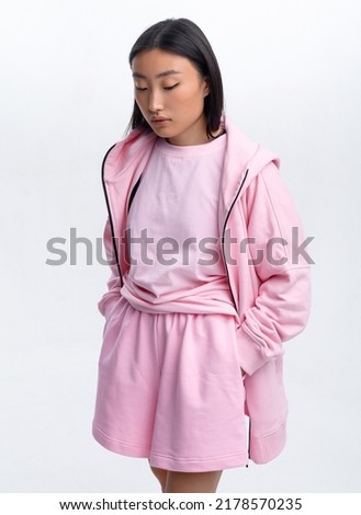 Beautiful Asian girl in a pink casual tracksuit posing against a white wall in a photo studio